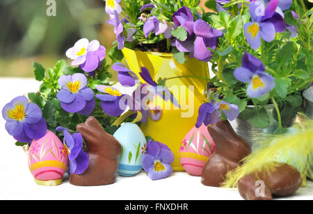 Il cioccolato e le uova di Pasqua tra i fiori su un tavolo in giardino Foto Stock