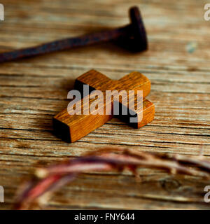 Primo piano di una piccola croce di legno, una raffigurazione della corona di spine di Gesù Cristo e di un chiodo su una superficie in legno Foto Stock