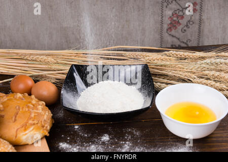 La cottura Ingredienti per la preparazione del pane con fresco Uova Rotte in una ciotola con la farina e il pane appena sfornato, formaggi bun, copia di spazio e di spighe di grano dietro. Foto Stock