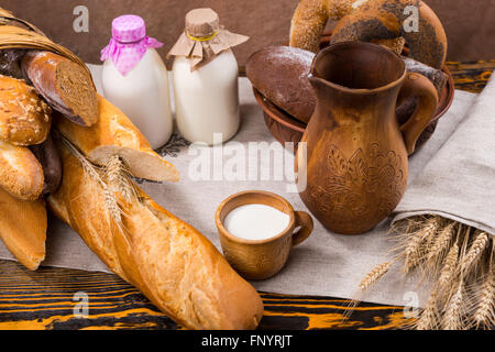 Piccola Coppa di legno di latte, tall brocca con secchi del grano culmi accanto a un vasto assortimento di prodotti di pane Foto Stock