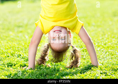 Kid girl standing capovolto sul suo capo su erba in estate Foto Stock