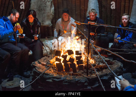 Salla, Lapponia, Finlandia. Persone renne di cottura soddisfino gli hamburger all'interno di in un tipico di capanne. Turf capanne sono molto essenziali e strutture Foto Stock