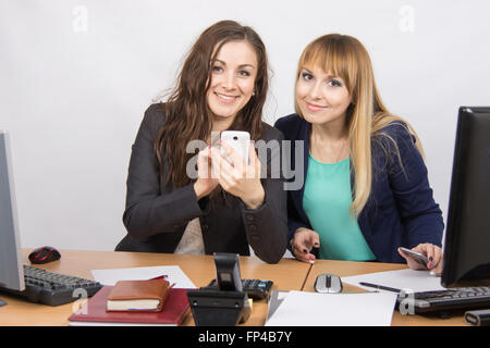 Due giovani dipendenti ufficio impegnato in affari privati in un telefono mobile alla sua scrivania Foto Stock