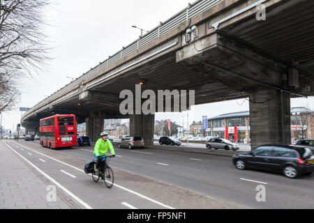 Il traffico sulla A4 su strada e un ciclista su una pista ciclabile con una sezione degli elevati autostrada M4 overhead, Brentford, London, England, Regno Unito Foto Stock