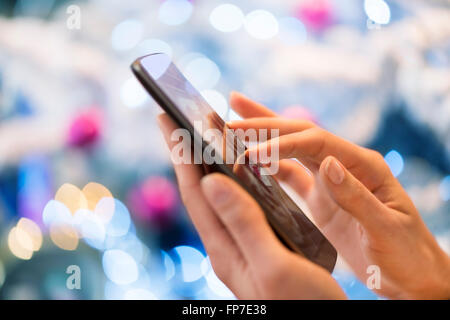 Donna che utilizza il suo telefono cellulare a casa. Boke albero di Natale sfondo; App,sms,chat,messaggio,e-mail,invio messaggi Foto Stock