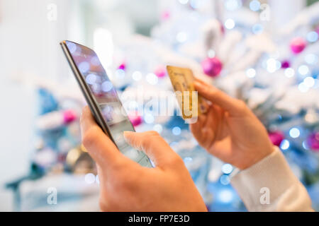Donna che utilizza il telefono cellulare e una carta di credito. Lo shopping online. Albero di Natale sfondo boke Foto Stock