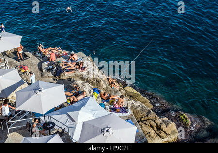 Ristorante Ombrelloni sulle rocce sotto le antiche mura della città di Dubrovnik in Croazia Foto Stock