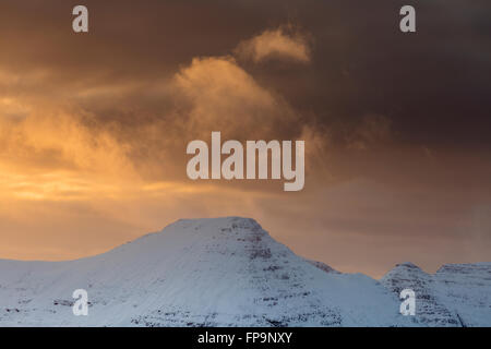 Illuminata luminosamente sopra le nuvole Beinn Dearg si stagliano contro uno sfondo scuro di nuvole di neve al tramonto, Torridon Foto Stock