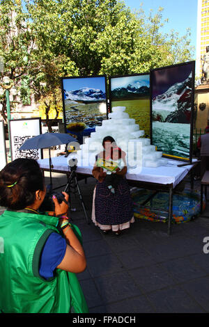 La Paz, Bolivia, 18 marzo 2016. Un lavoratore comunale prende le foto dei membri della holding pubblica cartelloni con modi per aiutare a proteggere l'ambiente nella parte anteriore della fusione dei blocchi di ghiaccio e le foto di Bolivia il montagne. La manifestazione è stata organizzata dalla La città di La Paz governo ad evidenziare il riscaldamento globale per Earth Hour (che avrà luogo domani). I ghiacciai in Bolivia e le Ande sono alcuni dei più veloci receding sul pianeta, causando cambiamenti ambientali e la scarsità di acqua in molte parti della regione. Credito: James Brunker / Alamy Live News Foto Stock