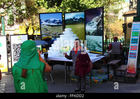 La Paz, Bolivia, 18 marzo 2016. Un lavoratore comunale prende le foto dei membri della holding pubblica cartelloni con modi per aiutare a proteggere l'ambiente nella parte anteriore della fusione dei blocchi di ghiaccio e le foto di Bolivia il montagne. La manifestazione è stata organizzata dalla La città di La Paz governo ad evidenziare il riscaldamento globale per Earth Hour (che avrà luogo domani). I ghiacciai in Bolivia e le Ande sono alcuni dei più veloci receding sul pianeta, causando cambiamenti ambientali e la scarsità di acqua in molte parti della regione. Credito: James Brunker / Alamy Live News Foto Stock