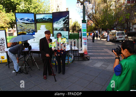 La Paz, Bolivia, 18 marzo 2016. Un lavoratore comunale prende le foto dei membri della holding pubblica cartelloni con modi per aiutare a proteggere l'ambiente nella parte anteriore della fusione dei blocchi di ghiaccio e le foto di Bolivia il montagne. La manifestazione è stata organizzata dalla La città di La Paz governo ad evidenziare il riscaldamento globale per Earth Hour (che avrà luogo domani). Credito: James Brunker / Alamy Live News Foto Stock