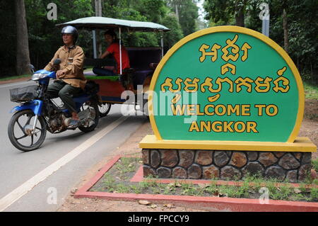 Un Tuk Tuk o remork attende vicino al 'bilingue Benvenuto a Angkor' firmare (sia in inglese e Khmer), Siem Reap Provincia, Cambogia. Credito: Kraig Lieb Foto Stock