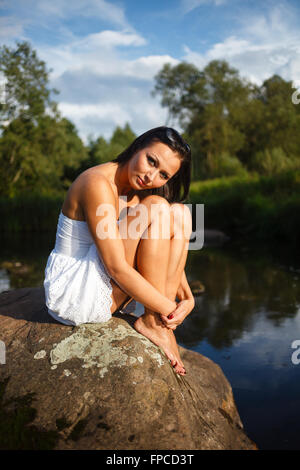 Bruna ragazza seduta su pietra. Foto Stock