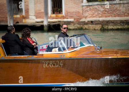 Barca-taxi skipper in una riva boat con due passeggeri sul Canal Grande di Venezia su una soleggiata giornata di primavera Foto Stock