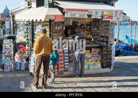 Tre clienti guardando e acquisto di carte su un tipico giornale italiano di stand a Venezia Foto Stock