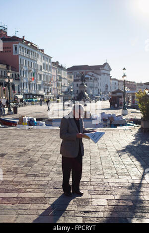 Uomo anziano leggendo il giornale di fronte al molo del traghetto sulla Riva degli Schiavoni quayside a Venezia in una giornata di primavera Foto Stock