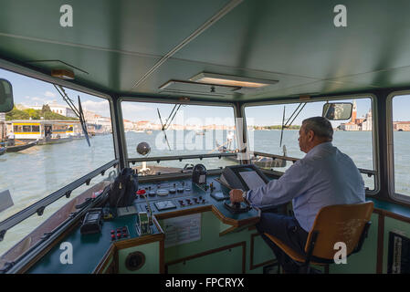 Skipper maschile seduto nella timoneria per la sterzatura del traghetto sul Canal Grande a Venezia in un pomeriggio soleggiato Foto Stock