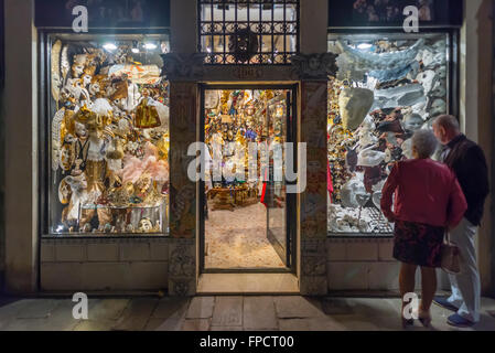 Un anziano giovane guardando la finestra illuminata di un negozio di vendita di maschere di carnevale a Venezia, Italia Foto Stock