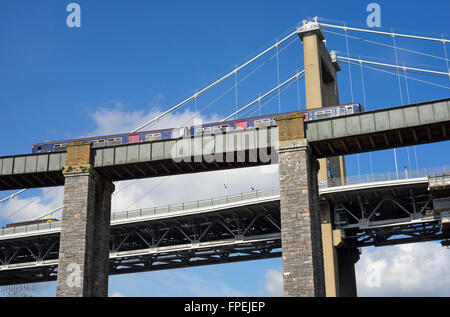 Il treno attraversa il Royal Albert ponte sopra il fiume Tamar sopra Saltash con la Tamar ponte stradale in background. Foto Stock