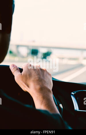 Primo piano di un giovane uomo caucasico, visto da dietro la guida di una vettura in una strada a più corsie Foto Stock