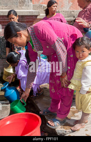 Il Nepal, Patan. Donna di riempimento brocca in plastica ad una fontana pubblica. Foto Stock