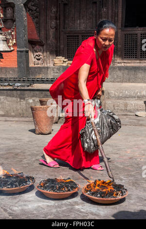 Il Nepal, Patan. Donna adoratore e offerte di fuoco al tempio indù. Foto Stock