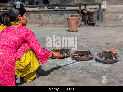 Il Nepal, Patan. Donna adoratore e offerte di fuoco al tempio indù. Foto Stock