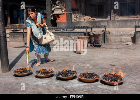 Il Nepal, Patan. Donna adoratore e offerte di fuoco al tempio indù. Foto Stock