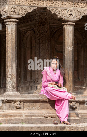 Il Nepal, Patan. Il nepalese giovane donna seduta sul bordo del tempio, Tika sulla sua fronte, telefono cellulare nelle sue mani. Foto Stock