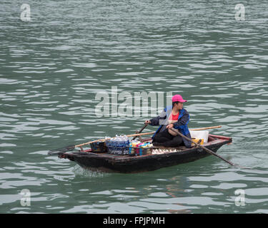 Halong Bay, Vietnam Una donna vietnamita nella sua barca a remi che vendono bevande e spuntini per i turisti nelle navi da crociera Foto Stock