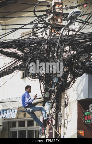 A Saigon, Vietnam - 20 Gennaio 2014: Elettricista fissaggio cavi disordinati sul montante del telefono. Foto Stock