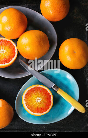 Affettato e tutto il sangue siciliano frutta di arancia sul turchese brillante e grigio di piastre in ceramica su sfondo nero, con kni vintage Foto Stock