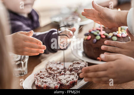 I bambini con le mani in mano cercando di toccare le scintille da un sparkler Foto Stock