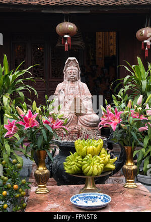 Il Buddha in un tempio vietnamita con offerte compresi i fiori e il fragrante mano gialla di Buddha frutta, Citrus medica Foto Stock