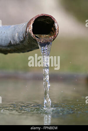 Acqua cristallina emergente dalla rusty vecchia tubazione. Simbolo per acqua limpida e nazione in via di sviluppo e la distribuzione di acqua ecc.. Foto Stock