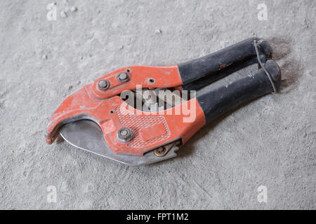 Red le forbici per il taglio di tubi in plastica sul pavimento in calcestruzzo Foto Stock