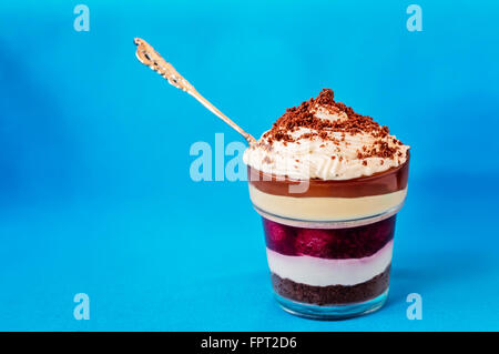 Layered dessert con biscotti sbriciolati topagainst su uno sfondo blu con cucchiaio d'argento Foto Stock