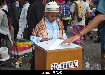 Un capretto inserito un po' di soldi in una carità scatola dopo Eid Al-Fitr preghiera di Makassar, Indonesia il 17 luglio 2015. Foto Stock