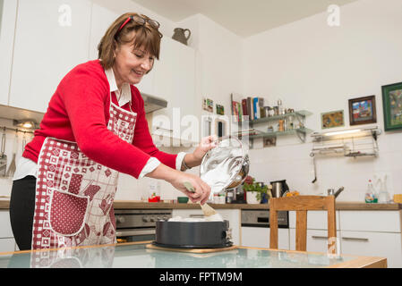 Senior donna versando la meringa su una torta base nella teglia, Monaco di Baviera, Germania Foto Stock