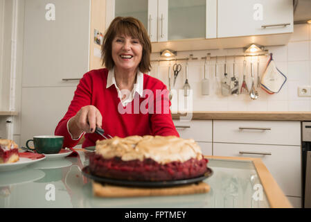 Donna Senior il taglio di una torta di meringa sul tavolo da pranzo in cucina, Baviera, Monaco di Baviera, Germania Foto Stock
