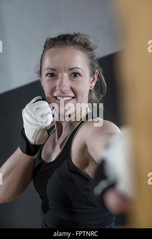 Giovane donna facendo forza di formazione mediante punzonatura sul punzone bag in palestra, Baviera, Germania Foto Stock