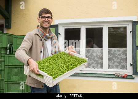 Ritratto di un agricoltore biologico tenendo un impianto gabbia per insalata in fattoria, Baviera, Germania Foto Stock