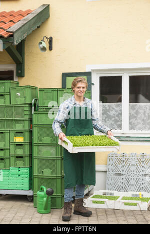 Ritratto di un agricoltore biologico tenendo un impianto gabbia per insalata in fattoria, Baviera, Germania Foto Stock