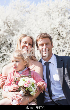 Sposa giovane con il loro figlio seduti di fronte blossom tree, Monaco di Baviera, Germania Foto Stock