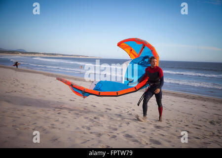 Giovane con kiteboard camminando sulla spiaggia di Viana do Castelo, Regione Norte, Portogallo Foto Stock