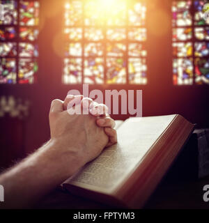 Mani giunte in preghiera in una Sacra Bibbia in una chiesa Foto Stock