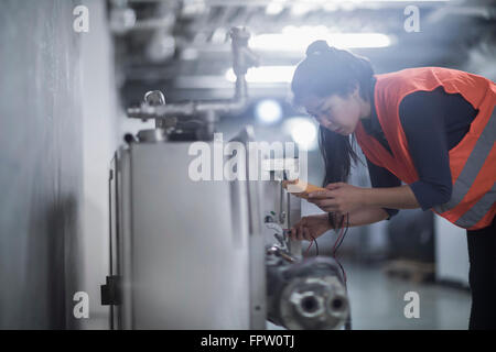 Giovane ingegnere femmina esaminando la macchina con il multimetro in un impianto industriale di Freiburg im Breisgau, Baden-Württemberg, Germania Foto Stock