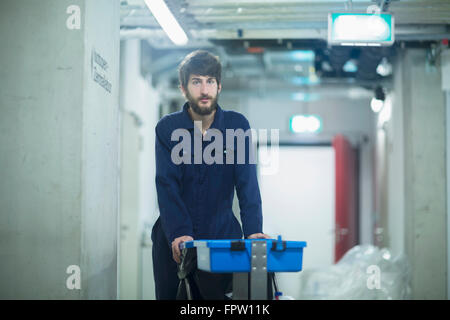 Giovane maschio di pulizia personale in piedi con cestino in un impianto industriale di Freiburg im Breisgau, Baden-Württemberg, Germania Foto Stock