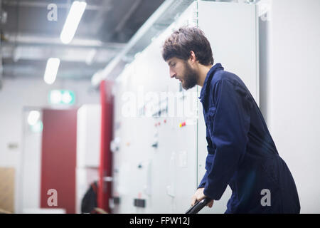 Giovane ingegnere maschio spingendo il carrello in un impianto industriale di Freiburg im Breisgau, Baden-Württemberg, Germania Foto Stock