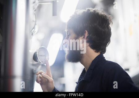 Giovane ingegnere maschio esaminando il manometro in un impianto industriale di Freiburg im Breisgau, Baden-Württemberg, Germania Foto Stock